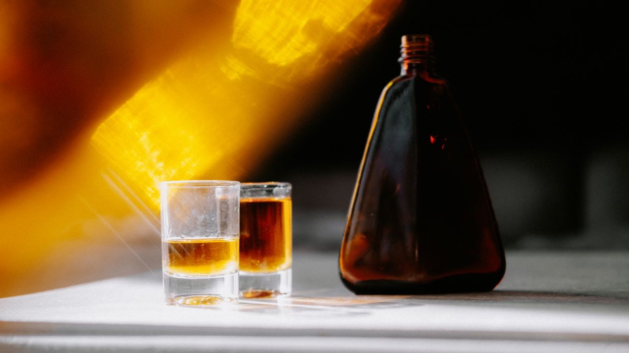A warm sunbeam highlights an amber bottle and glasses, creating a serene still life.