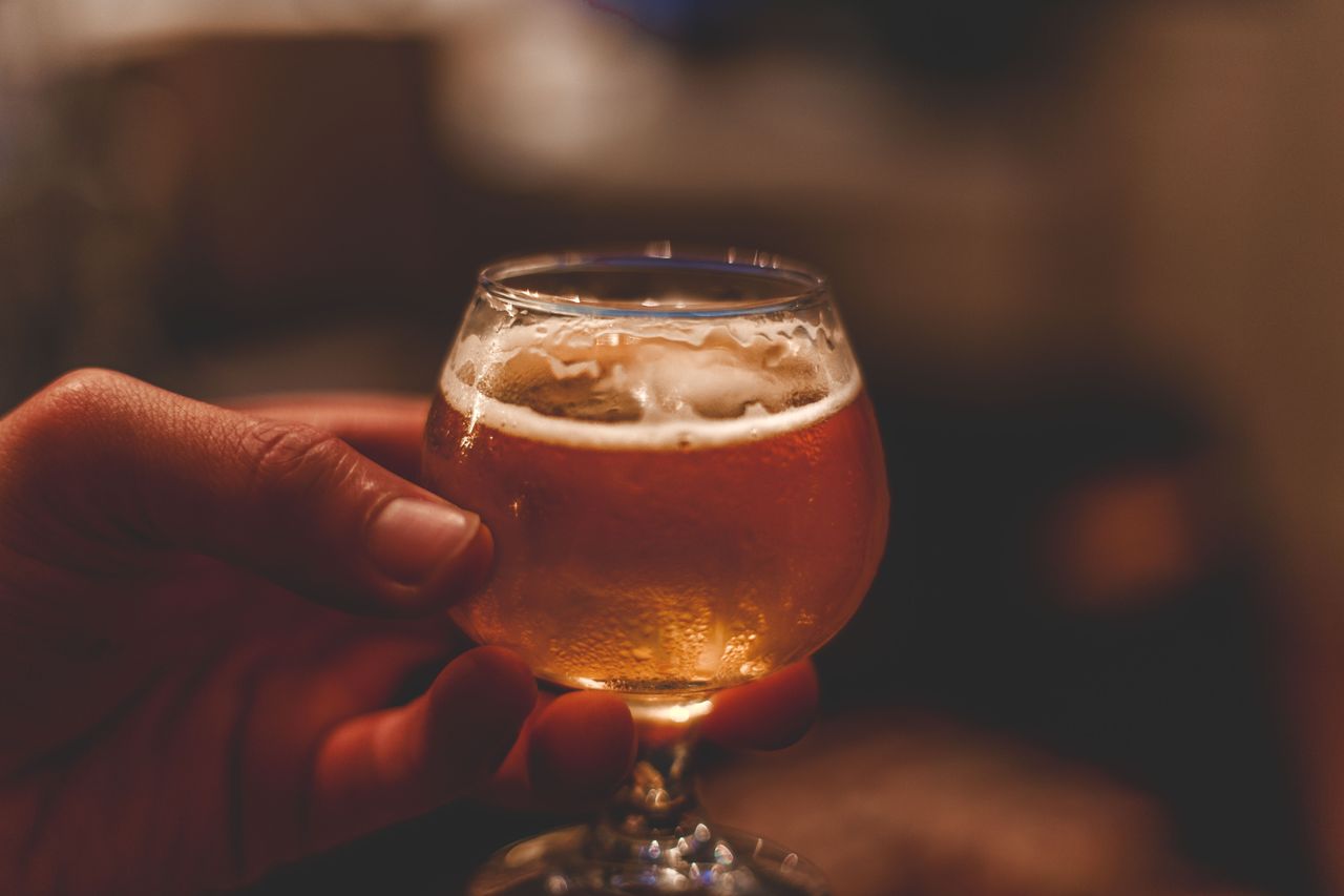 Vibrant close-up of a hand holding a foamy glass of ale indoors, perfect for celebration themes.