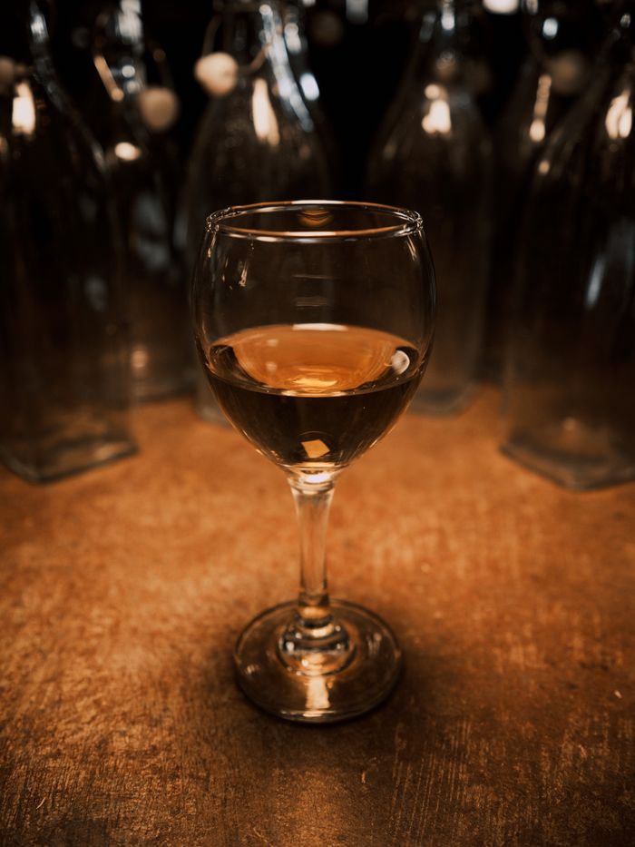 Elegant amber wine in a glass on a rustic table surrounded by empty bottles.