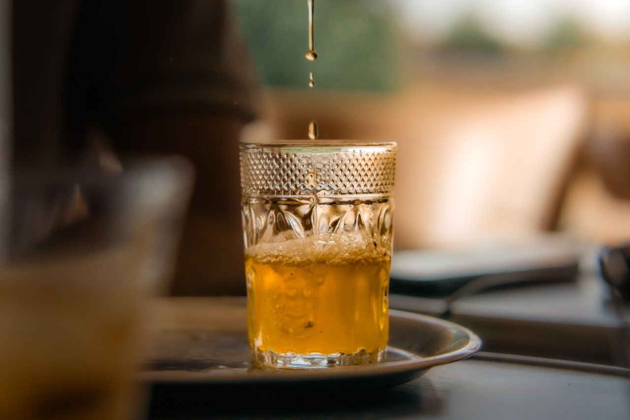 Close-up of a golden drink in an ornate glass with liquid pouring. Warm tones.